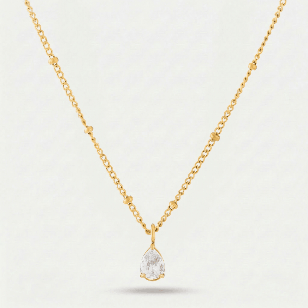 Collar Gota de Luz Amira dorado con piedra blanca sobre fondo claro