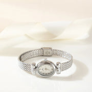 Reloj Ovalado Aurelia plateado sobre una superficie de color crema