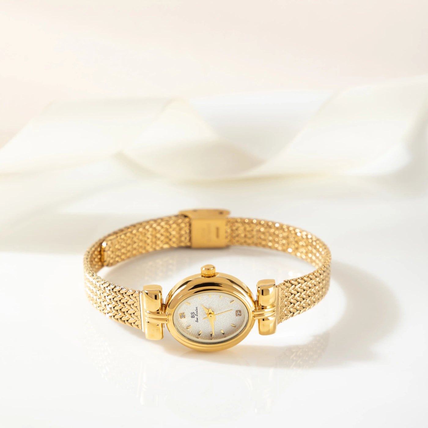 Reloj Ovalado Aurelia dorado sobre una superficie de color crema