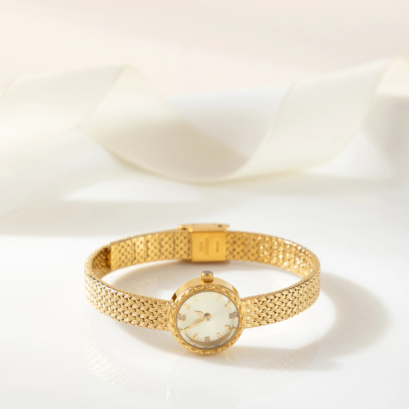 Reloj Malla Serena dorado sobre una superficie de color crema