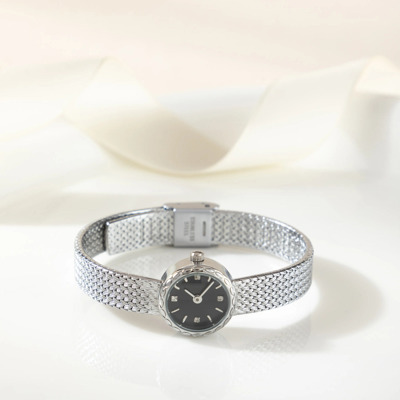 Reloj Malla Serena plateado sobre una superficie de color crema
