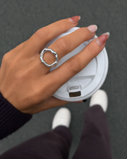 Anillo Círculo Eterno plateado en una mano sujetando una tapa de café