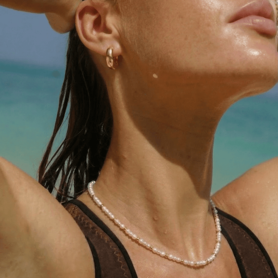 Mujer llevando el Collar Perlas Doradas Maelia junto al agua
